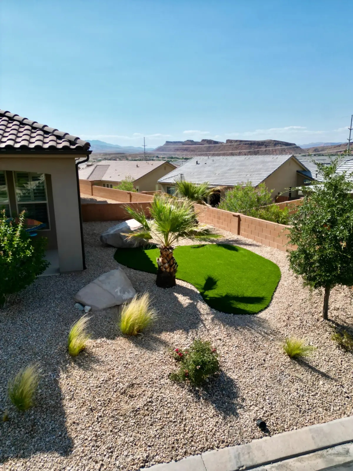 Desert landscape with a palm, boulders, and gravel beside a small turf lawn